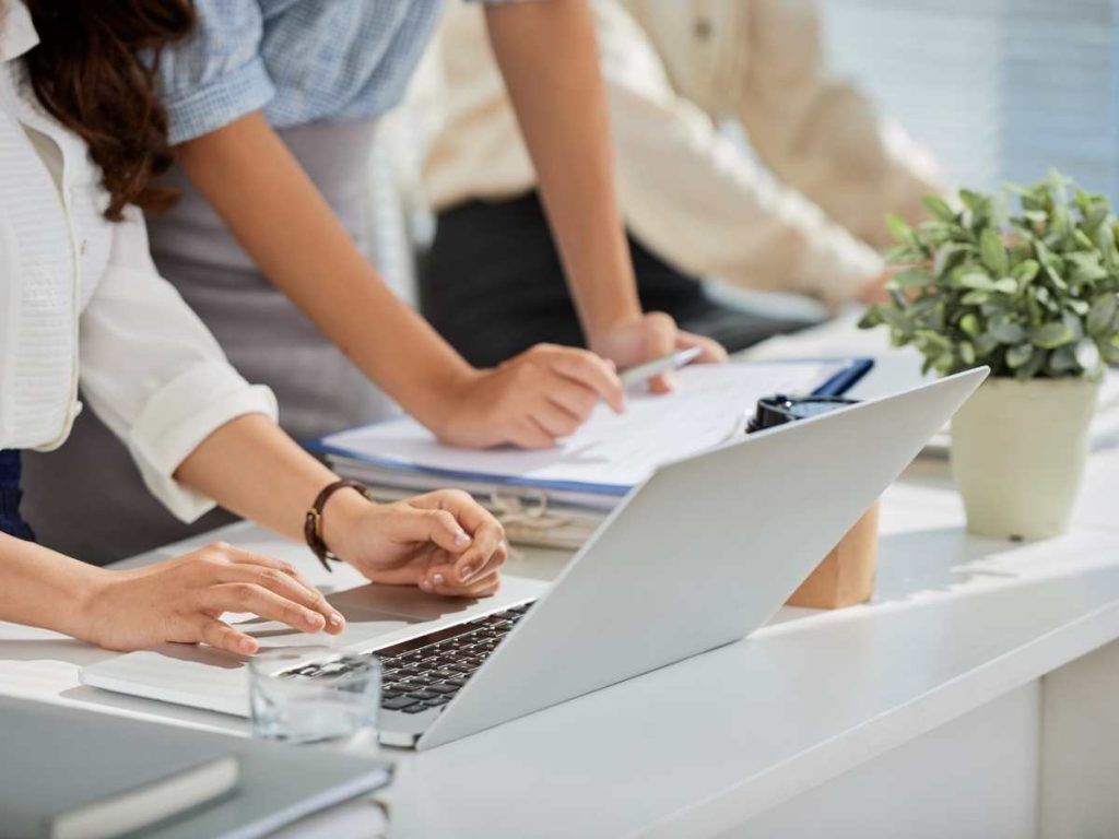 Duas pessoas trabalhando em um laptop com papéis ao redor, discutindo o índice de um doutorado.