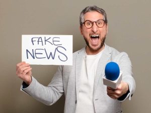 Homem segurando um cartaz com a mensagem "FAKE NEWS" e um microfone, ilustrando a importância de selecionar e redigir com qualidade uma tese de jornalismo.