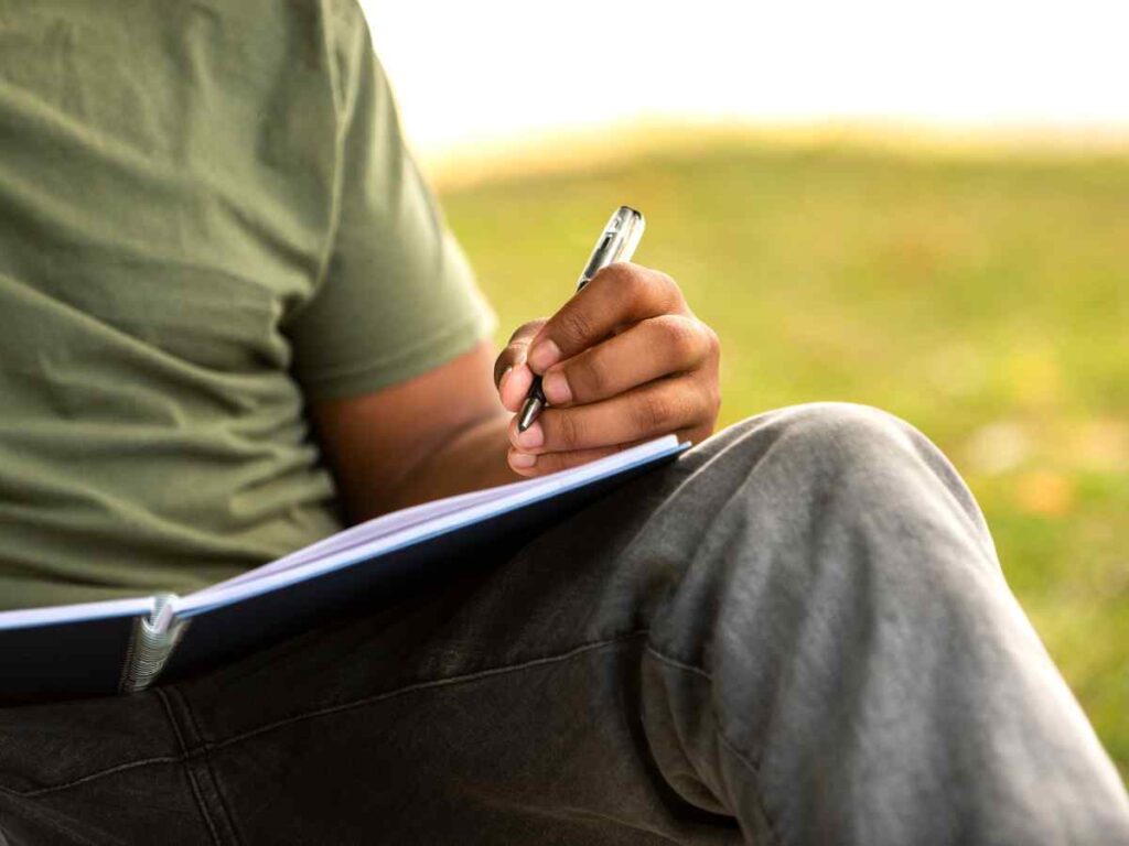 Pessoa a escrever num caderno ao ar livre.