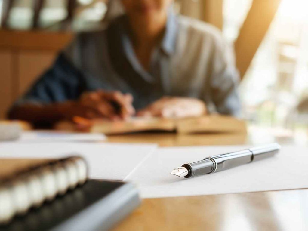 Estudante a trabalhar na sua tese numa mesa com uma caneta e livros em Coimbra.